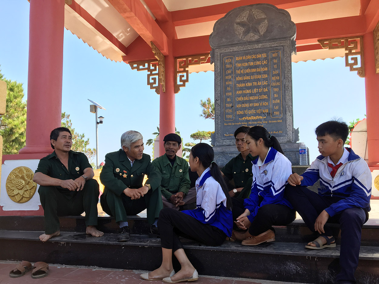 Các em học sinh xã Hơ Moong nghe cựu chiến binh kể chuyện về điểm cao 1015 và 1049 (ảnh: Khoa Điềm)