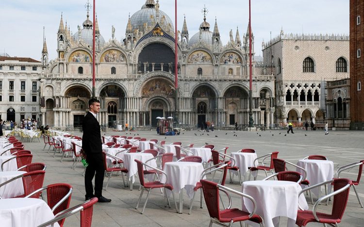 Một người phục vụ đứng cạnh những chiếc bàn trống bên ngoài một nhà hàng tại Quảng trường St Mark (Venice, Italy) ngày 9/3/2020. (Ảnh: REUTERS)