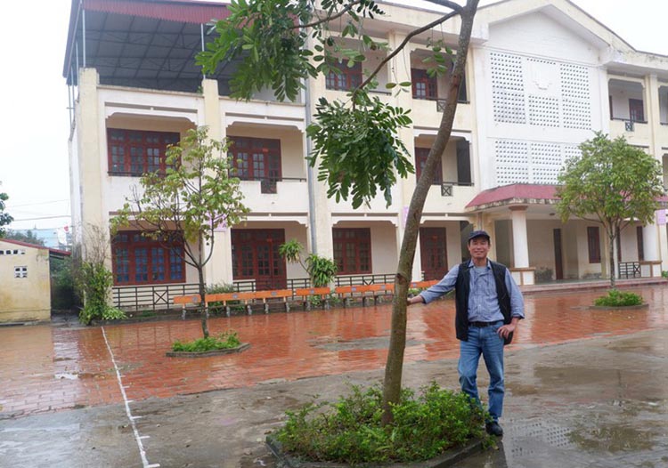 Ông Phạm Hùng Mạnh đứng bên gốc cây đã trồng cách đây vài năm tại sân trường Tiểu học Ngư Lộc 2, xã Ngư Lộc, huyện Hậu Lộc, tỉnh Thanh Hóa.