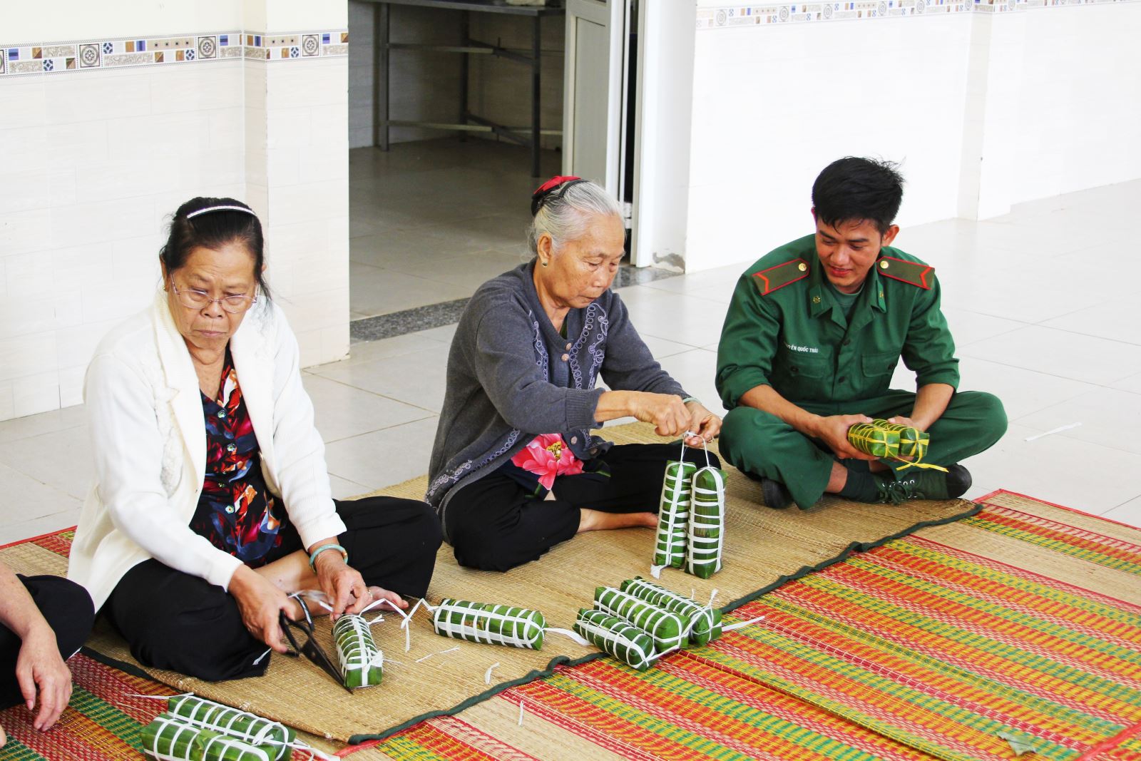 Chiến sĩ trẻ Nguyễn Quốc Thái đang được một mẹ hướng dẫn cách cột bánh.